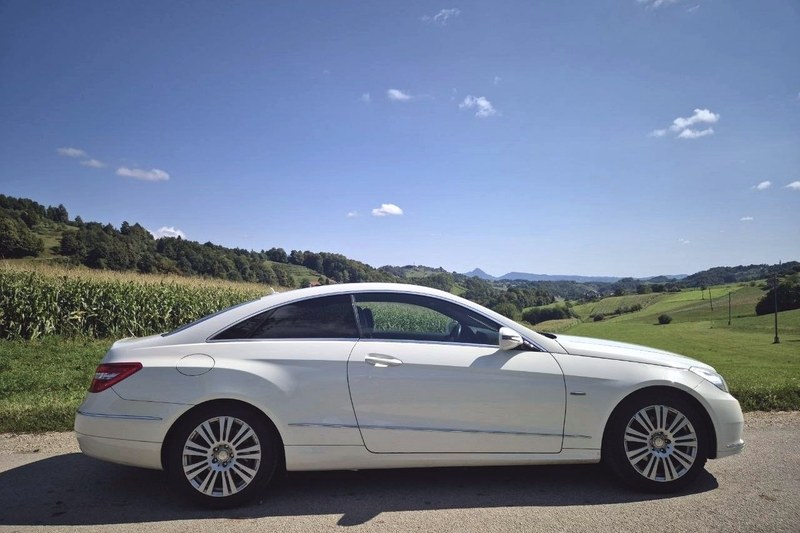 Белый Mercedes E-Class купе TourSlo сбоку, среди холмов